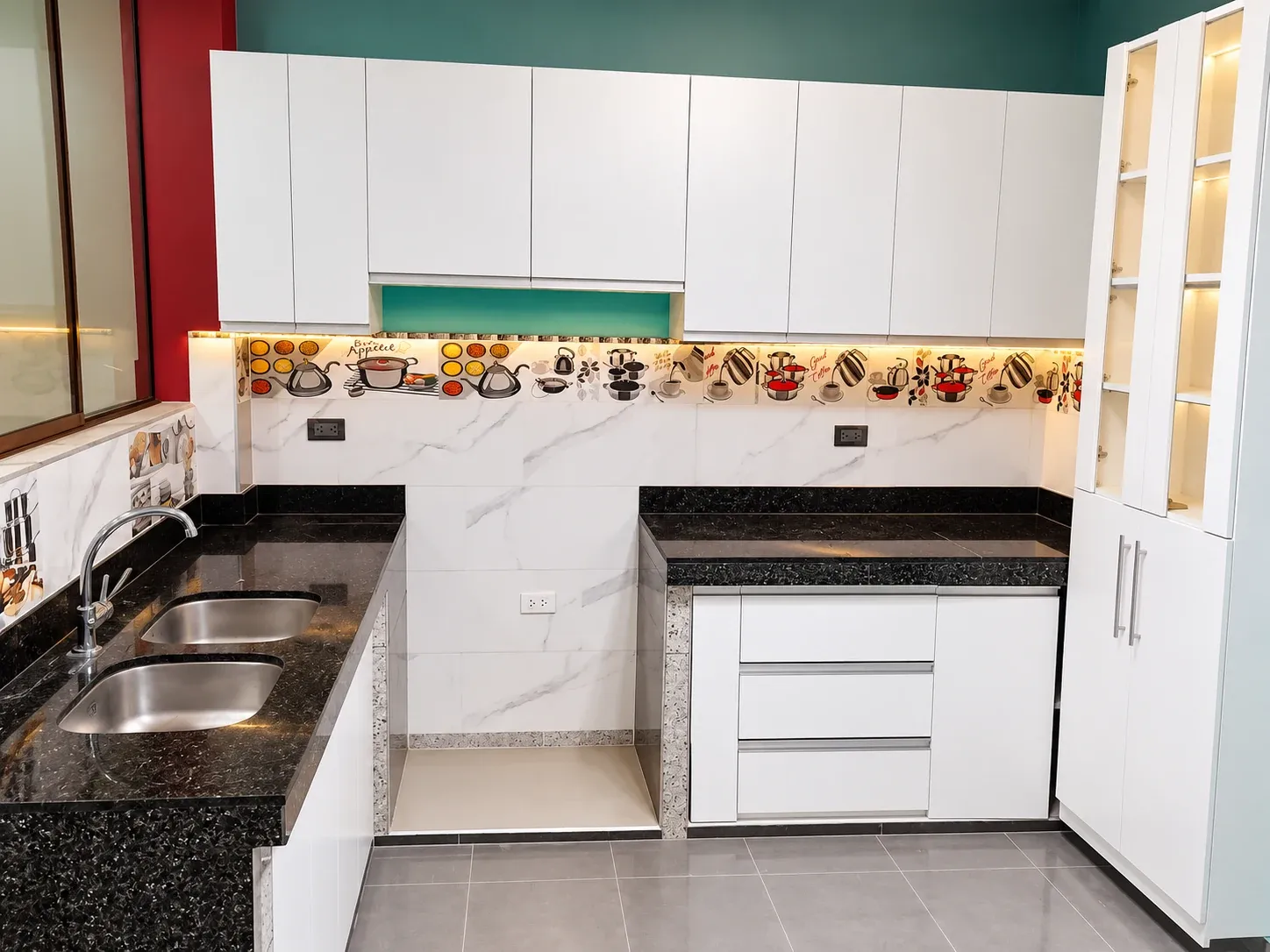 Cocina blanca con encimera oscura, lavadero doble y vitrina vertical frente a una pared superior verde.