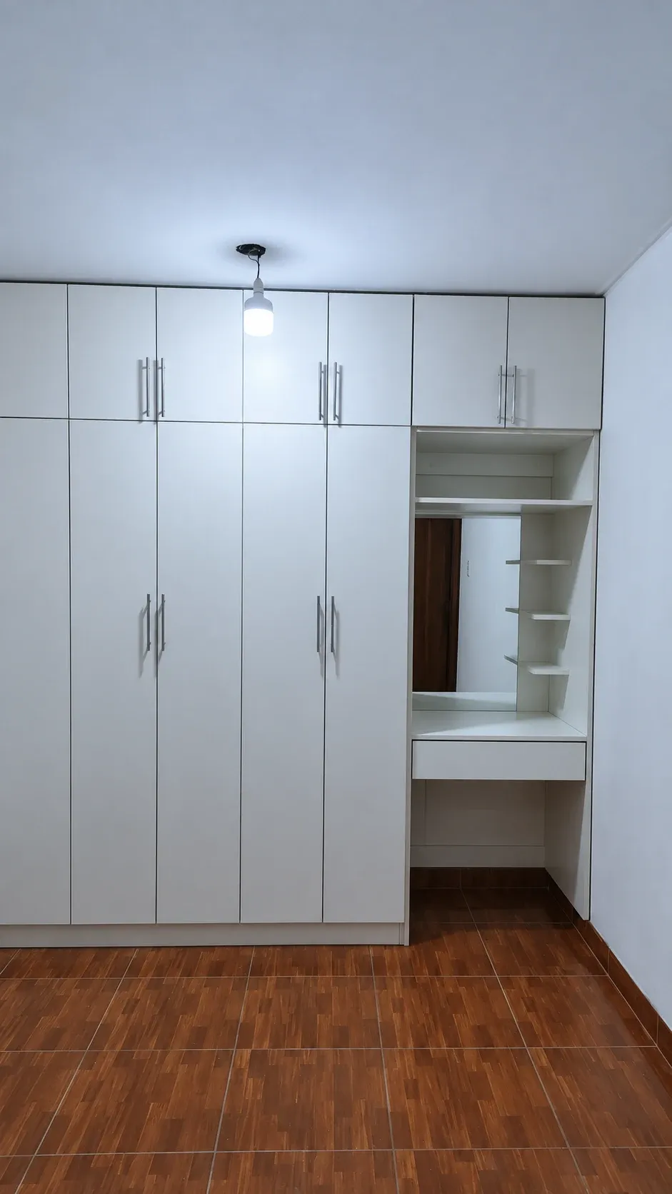 Clóset blanco cerrado con puertas abatibles, compartimentos superiores y tocador con espejo y estantes laterales.