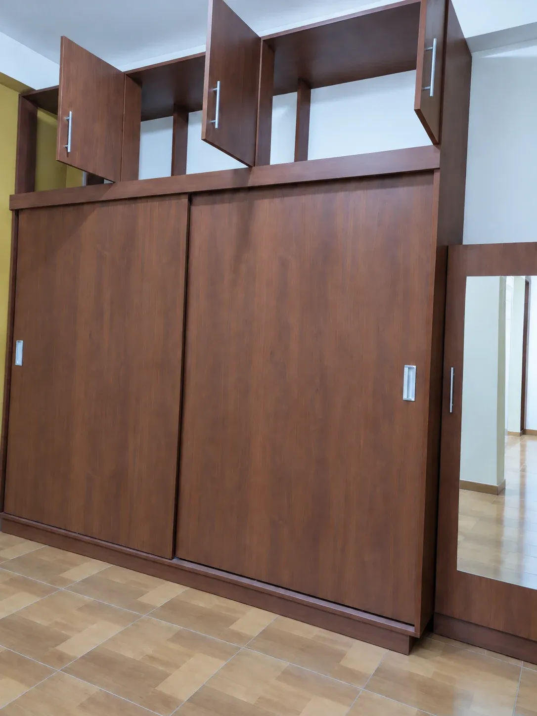 Clóset con acabado madera, puertas corredizas cerradas, puertas superiores abiertas y espejo lateral.